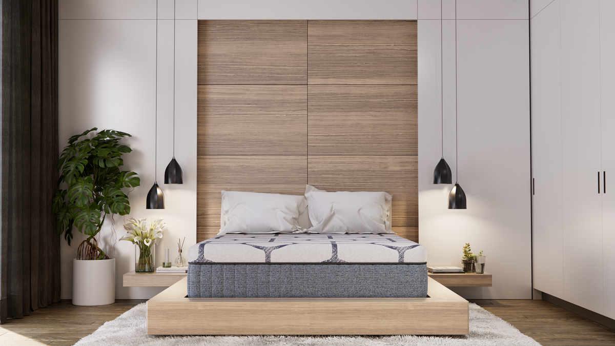 A new quilted queen mattress on a low light-wood platform bed in a calm neutral bedroom, seen from the foot of the bed with the mattress side panel visible