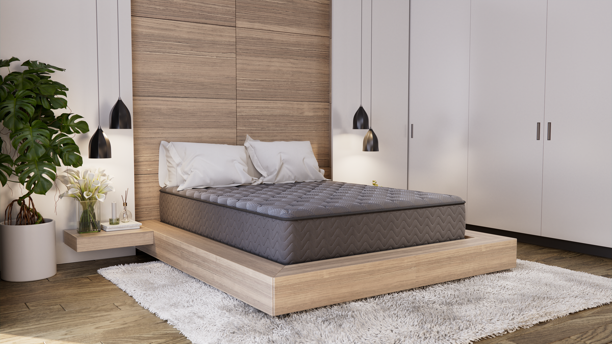 A charcoal tight-top quilted queen mattress on a low light-wood platform bed in a calm neutral bedroom, seen from the foot of the bed