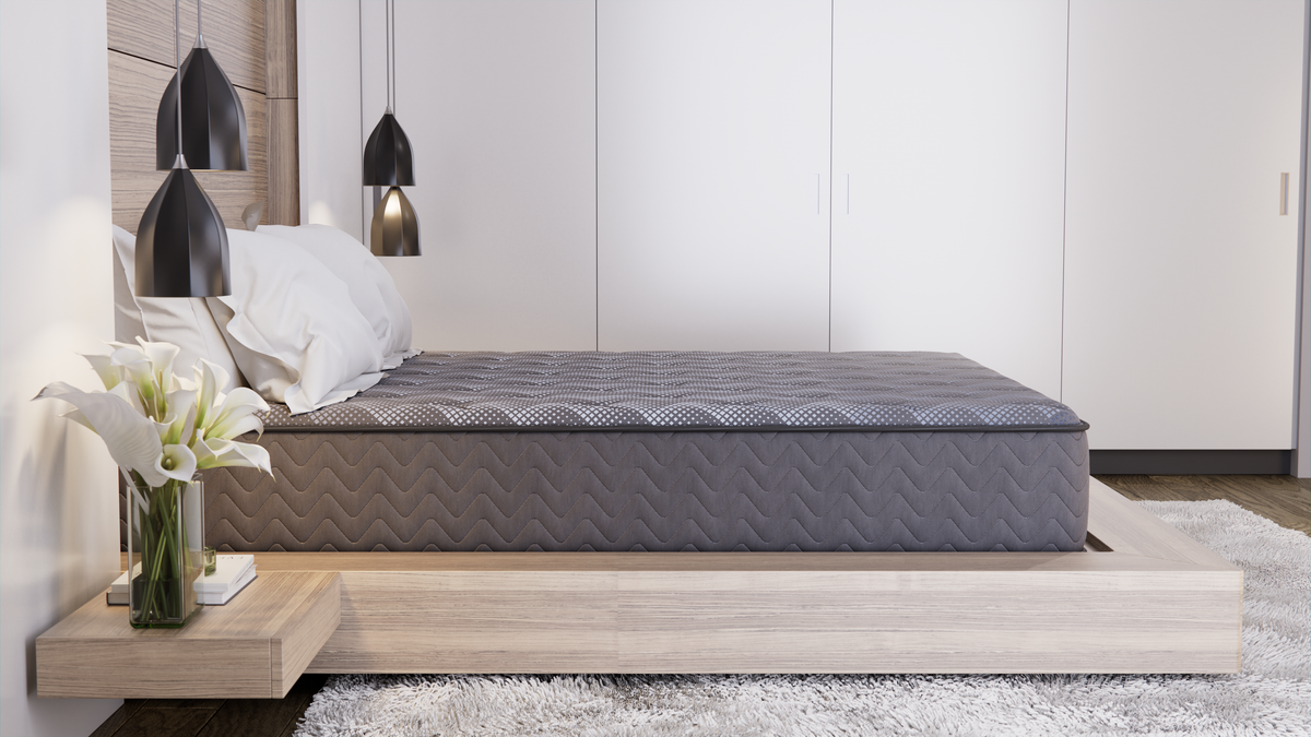 A charcoal quilted tight-top queen mattress on a low light-wood platform base in a calm neutral bedroom with white wardrobes, black pendant lights and a white rug