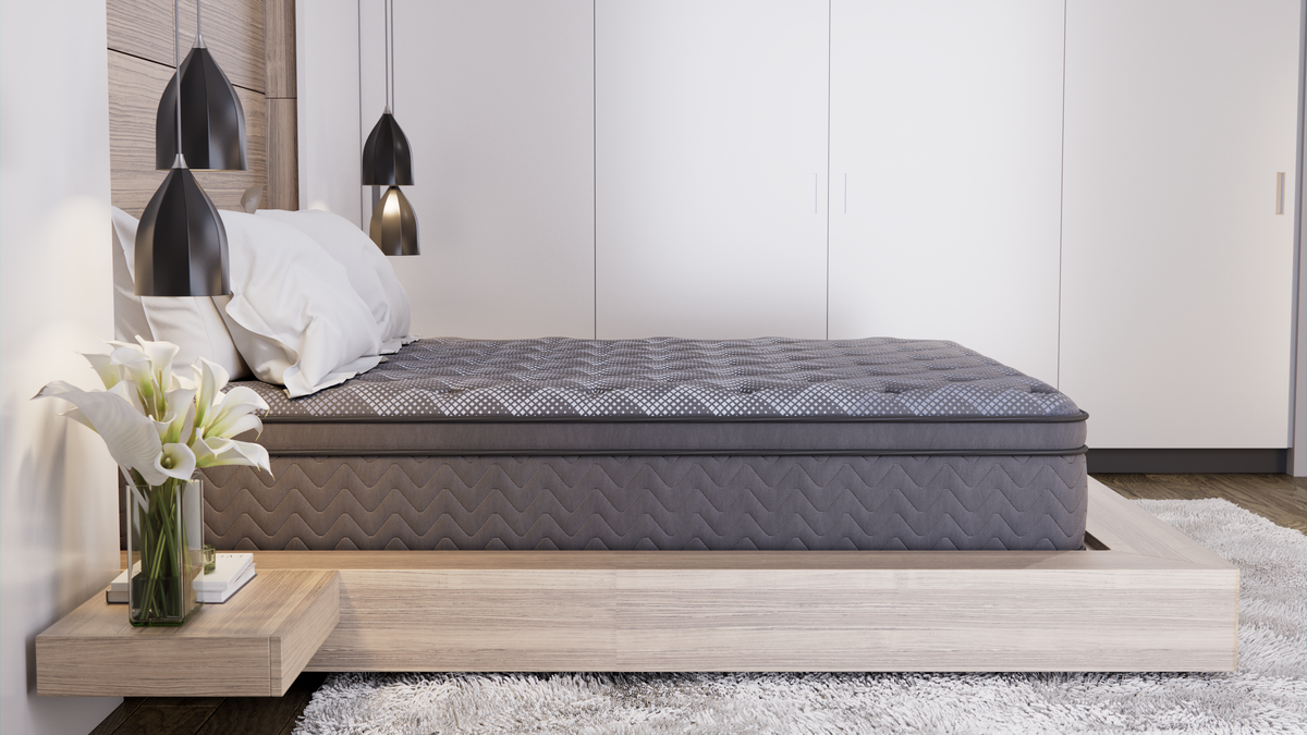 A grey quilted pillowtop queen mattress on a low light-wood platform base in a calm neutral bedroom with white wardrobes and pendant lights