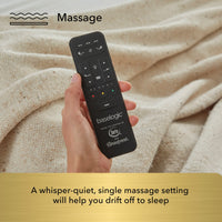 Hand holding a black remote control with 'baselogic' branding against a beige fabric background.