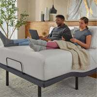 Two people sitting on a bed using electronic devices in a cozy room.