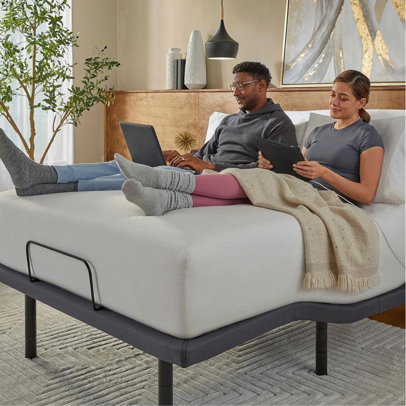 Two people sitting on a bed using electronic devices in a cozy room.
